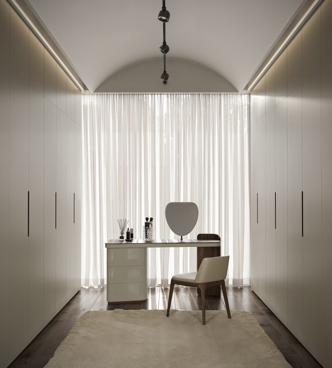 Minimalist dressing room with built-in wardrobes, a vanity table with mirror, and a comfortable chair, illuminated by natural light through sheer curtains.