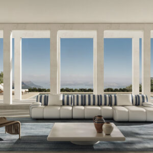 Modern living room with large floor-to-ceiling windows showcasing a scenic mountain view, featuring a stylish white sofa with blue striped cushions, a wooden chair, and a minimalist coffee table.