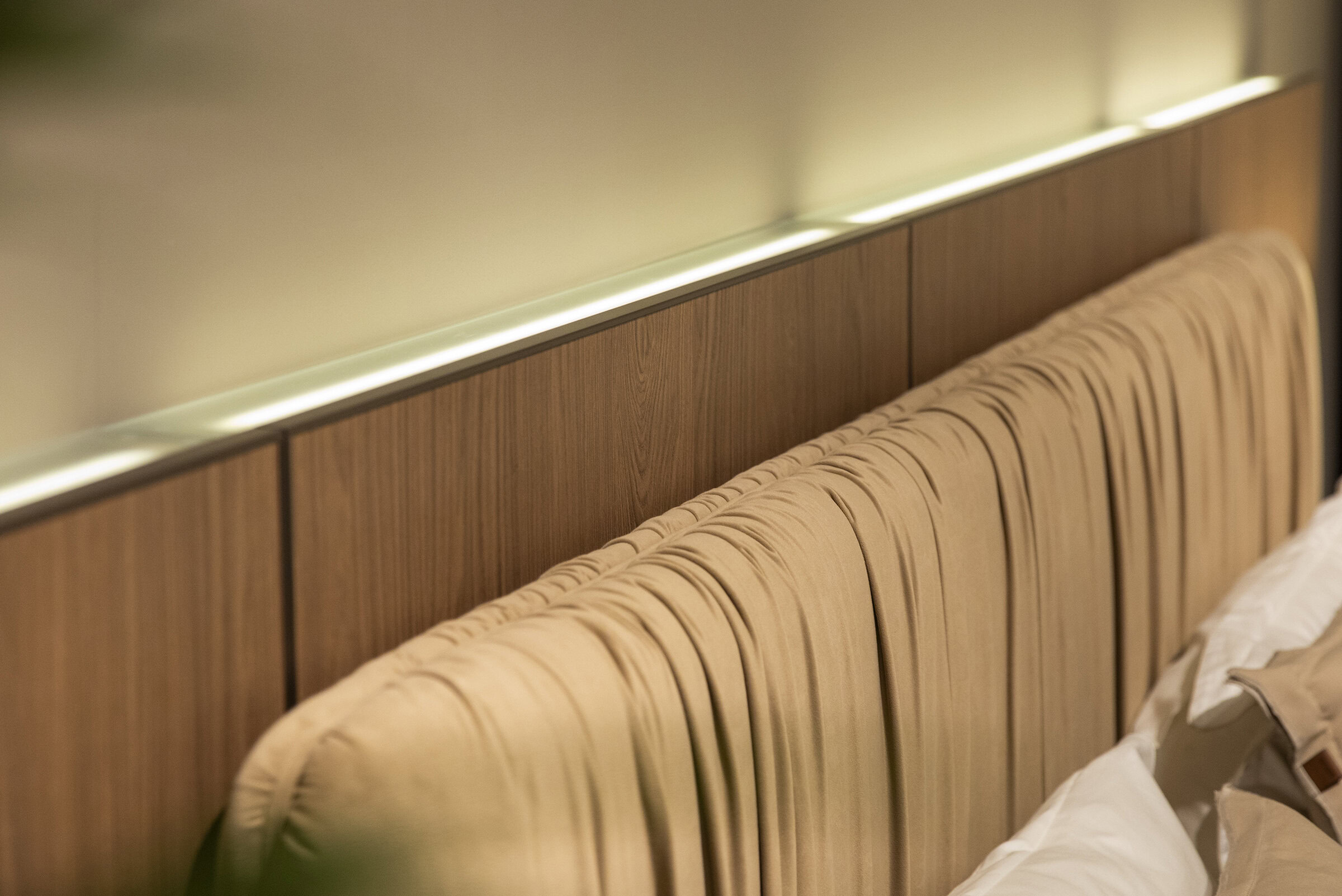 Luxurious wooden upholstered headboard with ambient lighting, perfect for modern bedroom decor, combining comfort and style in premium Saloni Furniture designs.