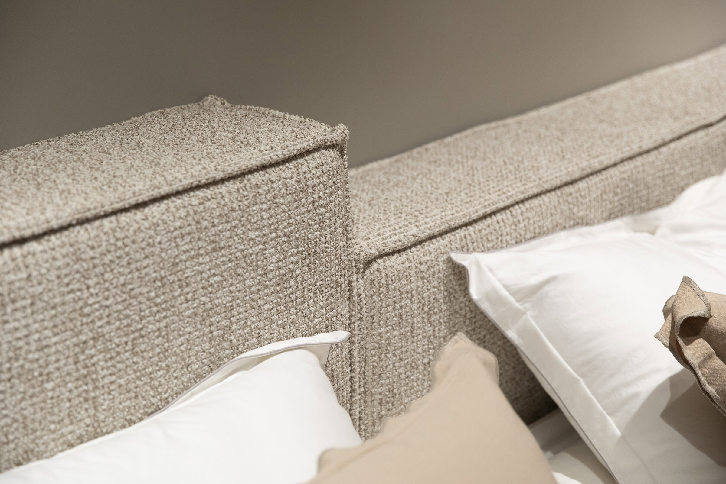 Luxurious beige upholstered bed headboard with textured fabric and padding, paired with white and beige pillows for a cozy and elegant bedroom decor.