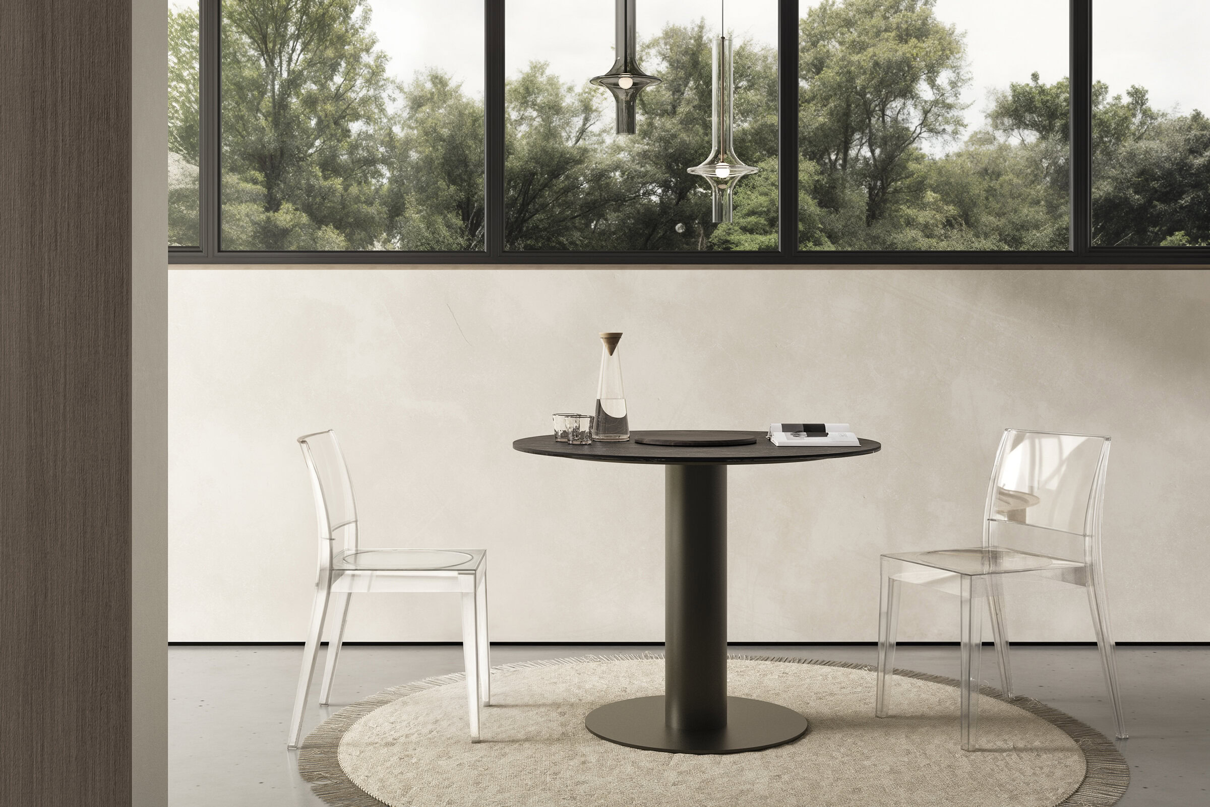 Masă rotundă modernă, cu blat negru elegant și bază robustă, asortată cu scaune din acrilic transparent, amplasată lângă ferestre mari cu o priveliște luxuriantă asupra unui peisaj verde, exemplificând designul minimalist contemporan de mobilier.