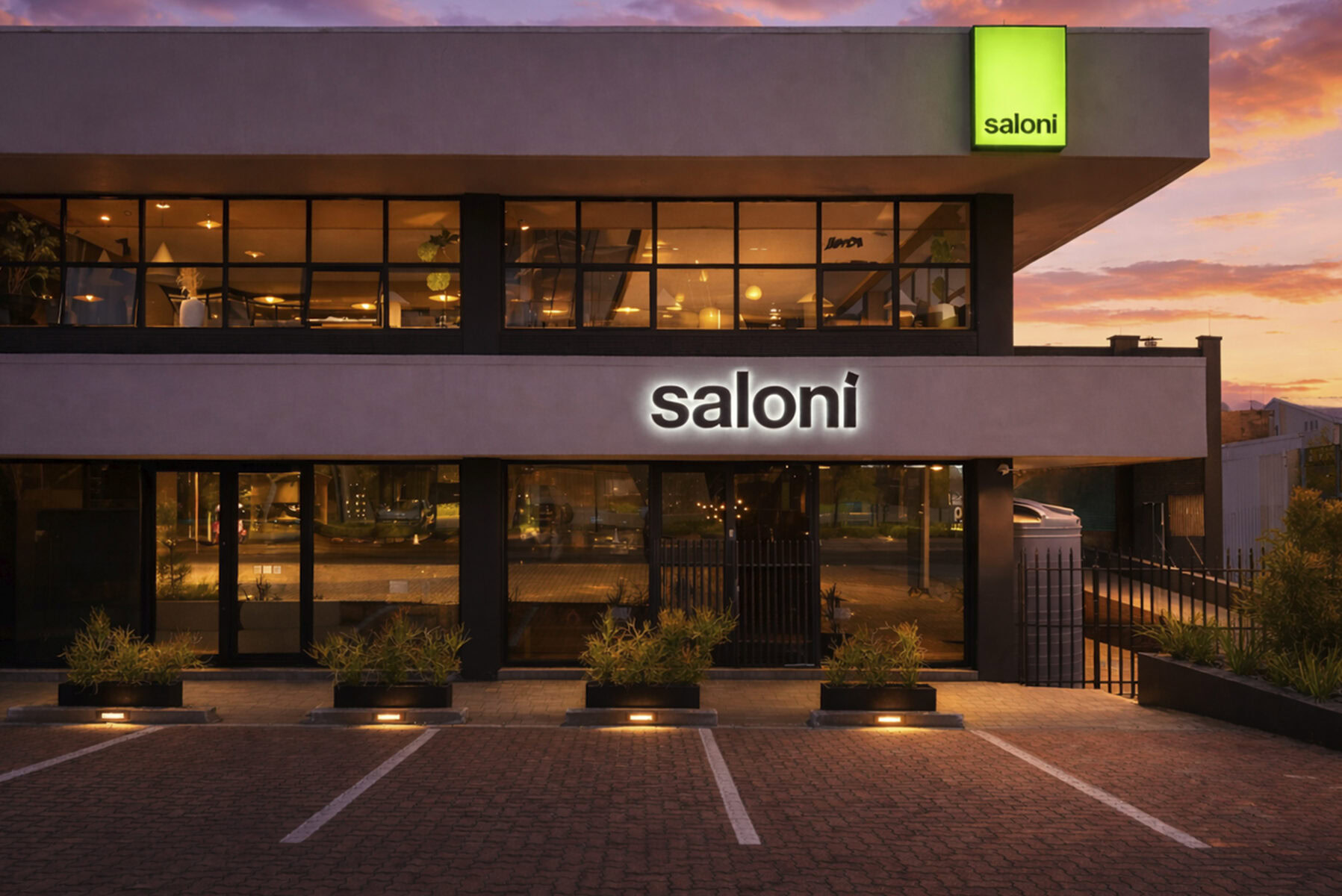 Saloni furniture store facade with large glass windows showcasing stylish furniture displays, illuminated at dusk, highlighting contemporary design and inviting shopping ambiance.